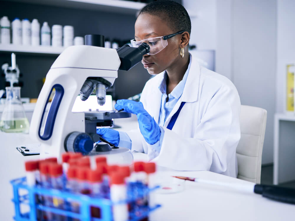 A female scientist in a laboratory uses a microscope to analyze a blood sample.